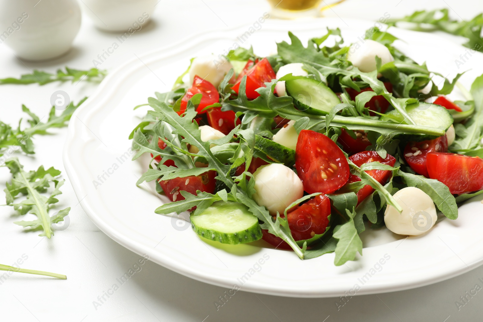 Photo of Tasty salad with arugula, mozzarella, tomatoes and cucumber on white table, closeup