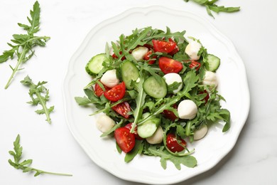 Photo of Tasty salad with arugula, mozzarella, tomatoes and cucumber on white marble table, flat lay