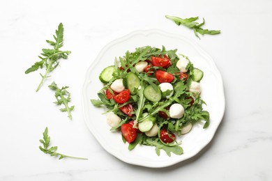 Photo of Tasty salad with arugula, mozzarella, tomatoes and cucumber on white marble table, flat lay