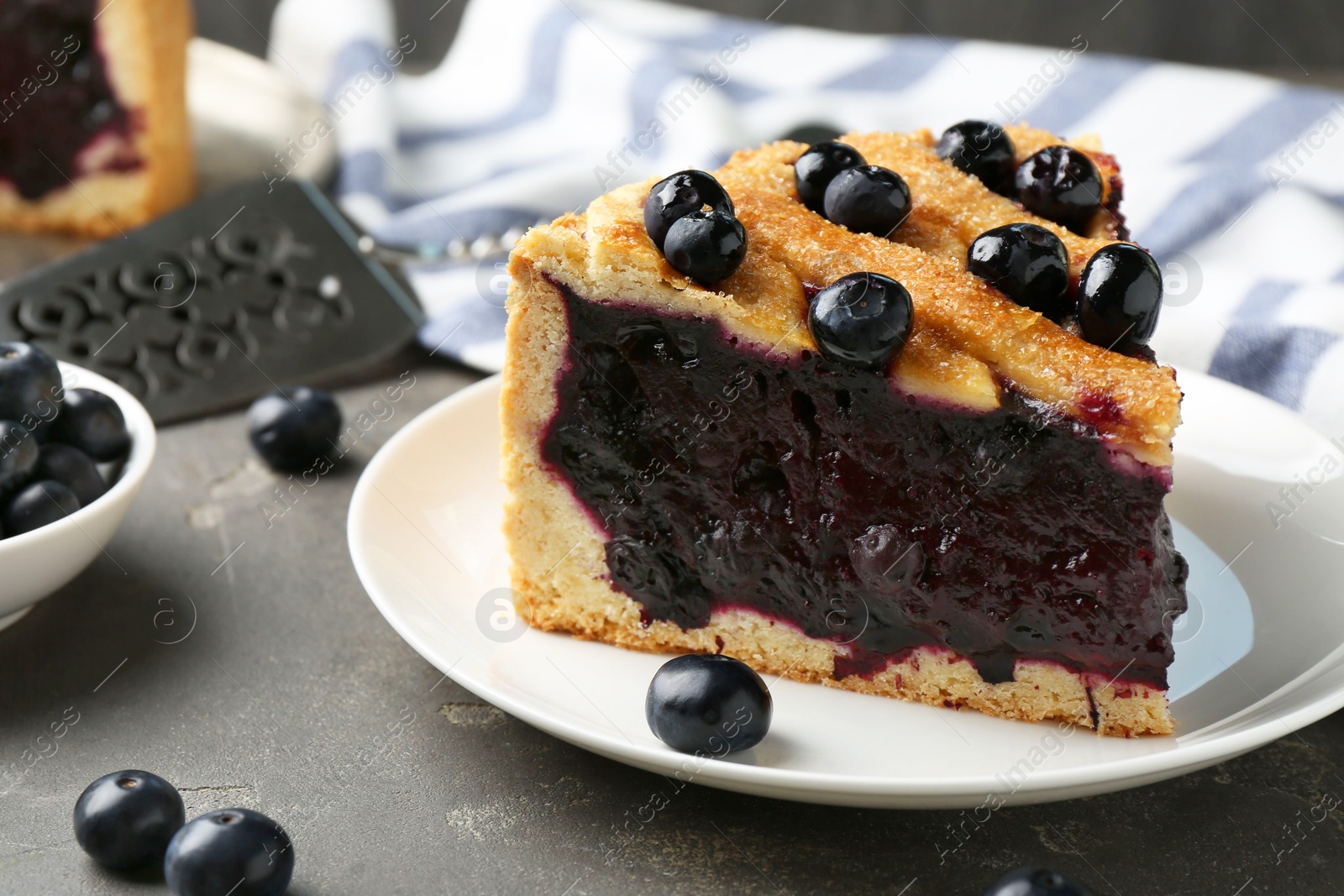 Photo of Slice of delicious homemade blueberry pie served on grey table, closeup