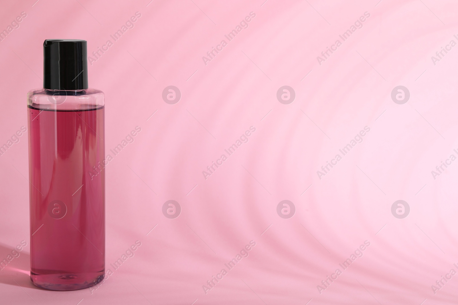 Photo of Shampoo in bottle on pink background, space for text