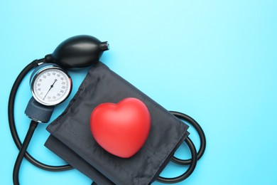 Photo of Blood pressure measuring device and squeeze heart on light blue background, top view. Space for text