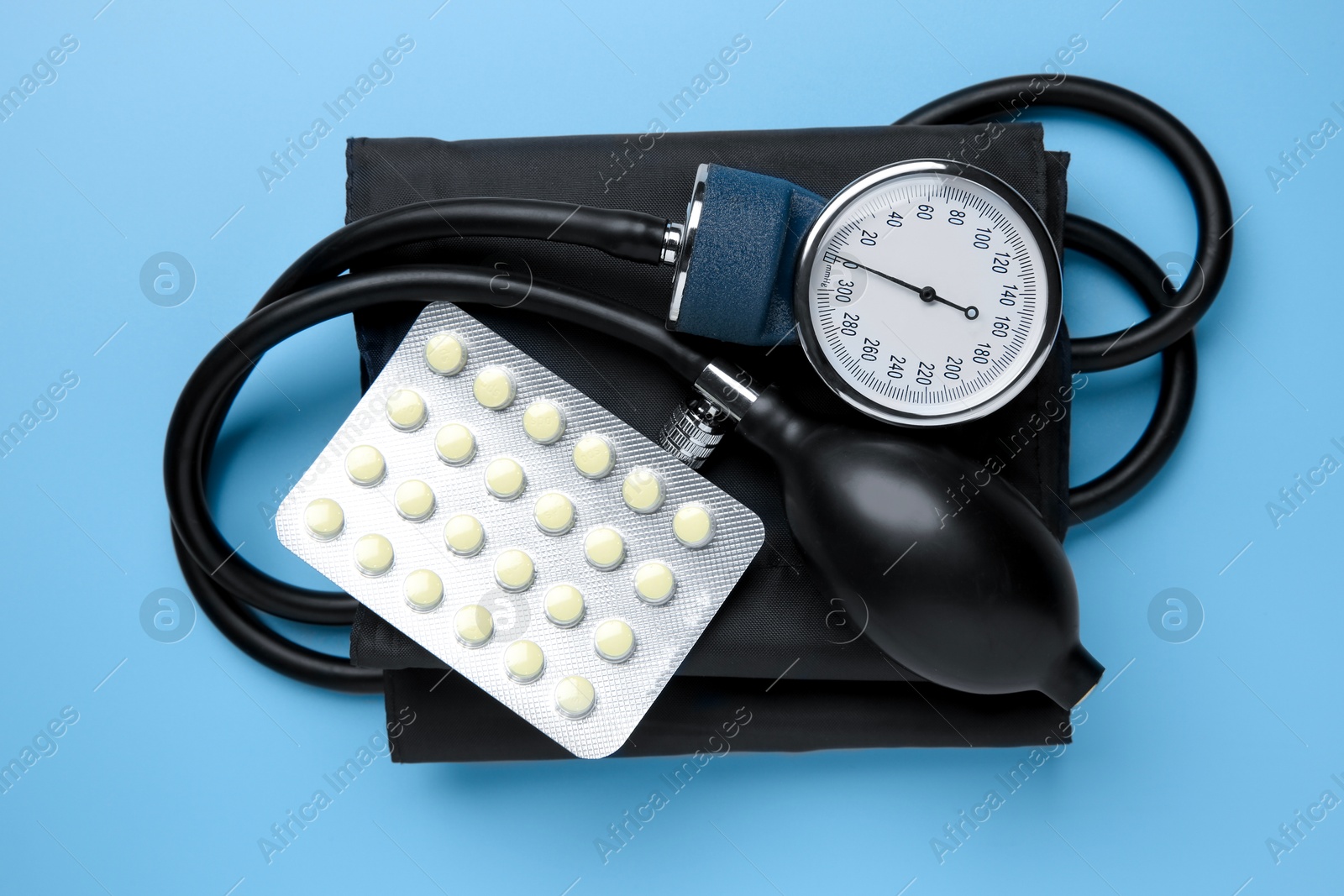 Photo of Blood pressure measuring device and pills on light blue background, top view