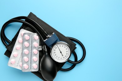 Photo of Blood pressure measuring device and pills on light blue background, top view