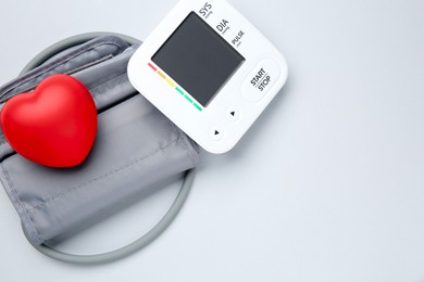 Blood pressure measuring device and squeeze heart on light grey background, top view. Space for text