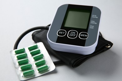 Photo of Blood pressure measuring device and pills on light grey background, closeup