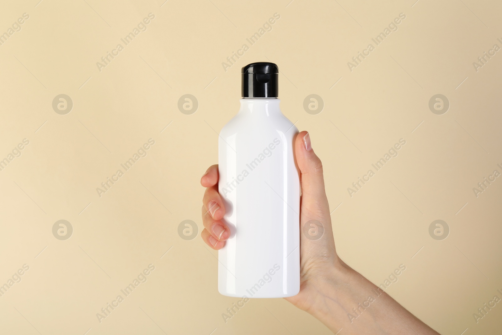 Photo of Woman with shampoo bottle on beige background, closeup