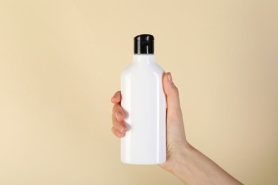 Photo of Woman with shampoo bottle on beige background, closeup