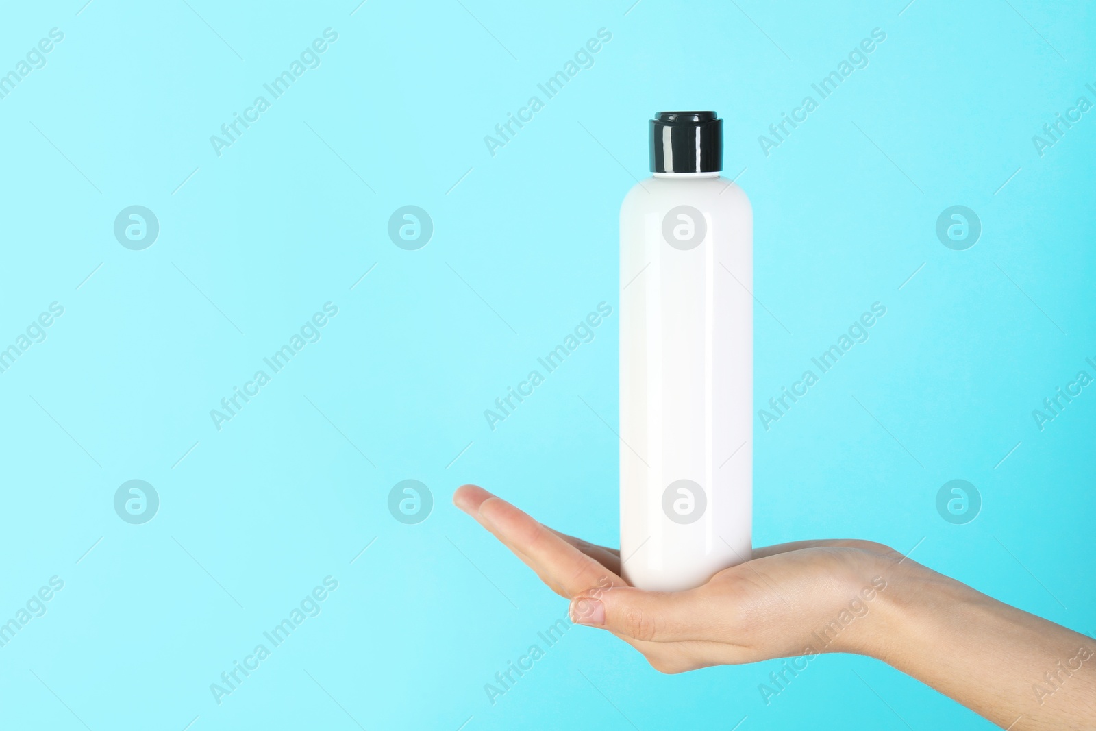 Photo of Woman with shampoo bottle on light blue background, closeup. Space for text