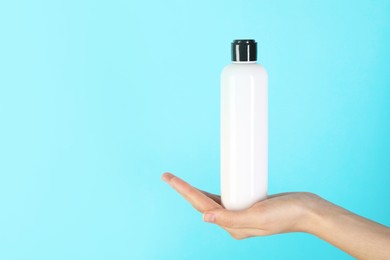 Photo of Woman with shampoo bottle on light blue background, closeup. Space for text