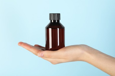 Woman with shampoo bottle on light blue background, closeup