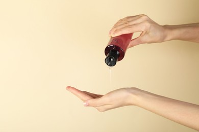 Photo of Woman pouring shampoo onto hand on beige background, closeup. Space for text