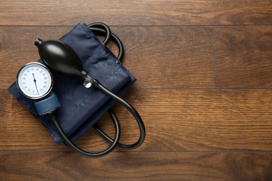 Photo of Blood pressure measuring device on wooden table, top view. Space for text