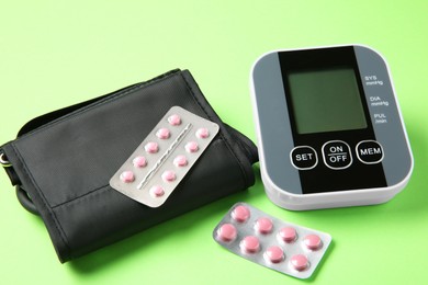 Blood pressure measuring device and pills on green background, closeup