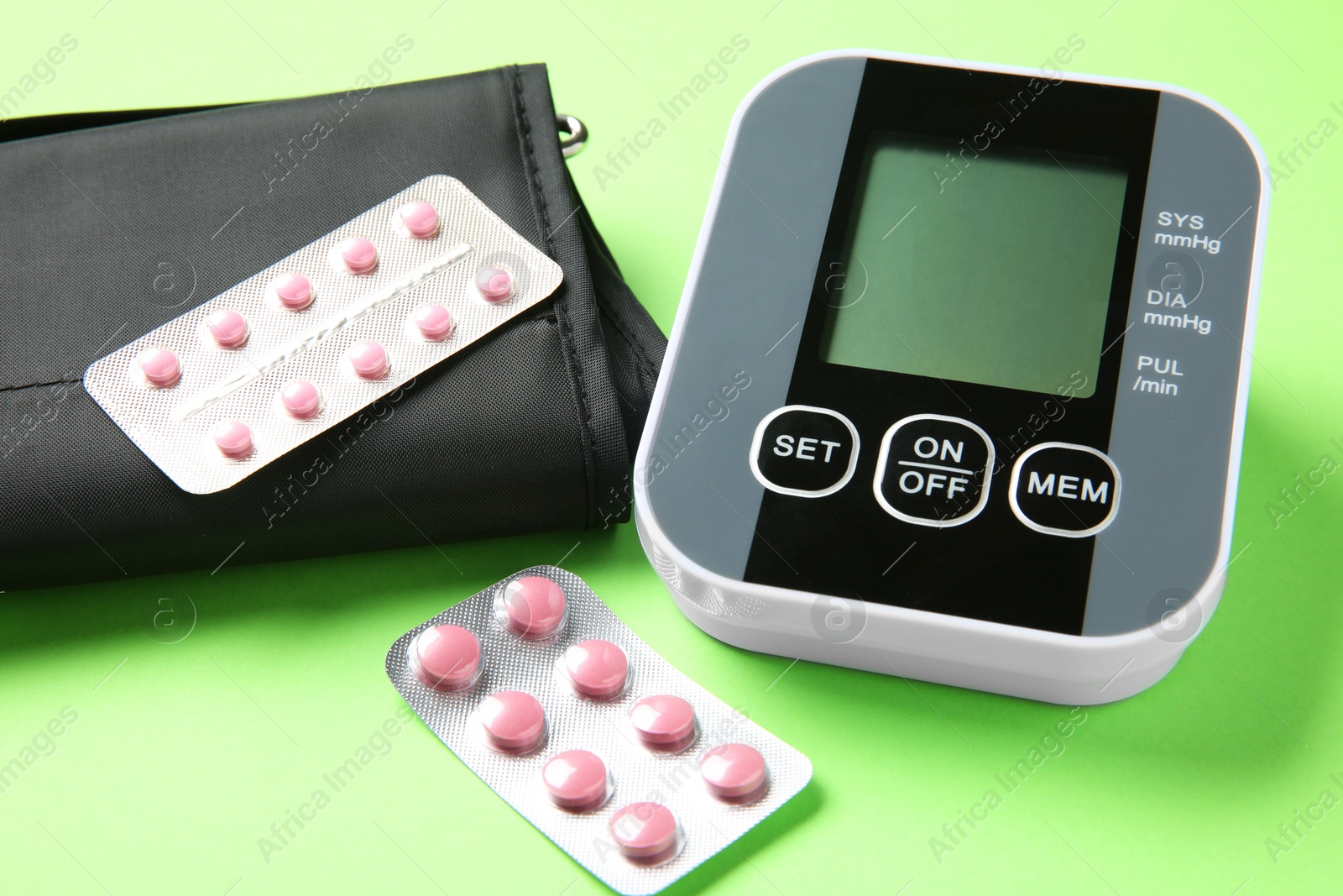 Photo of Blood pressure measuring device and pills on green background, closeup