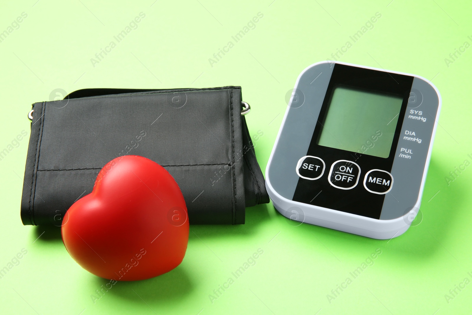 Photo of Blood pressure measuring device and squeeze heart on green background, closeup