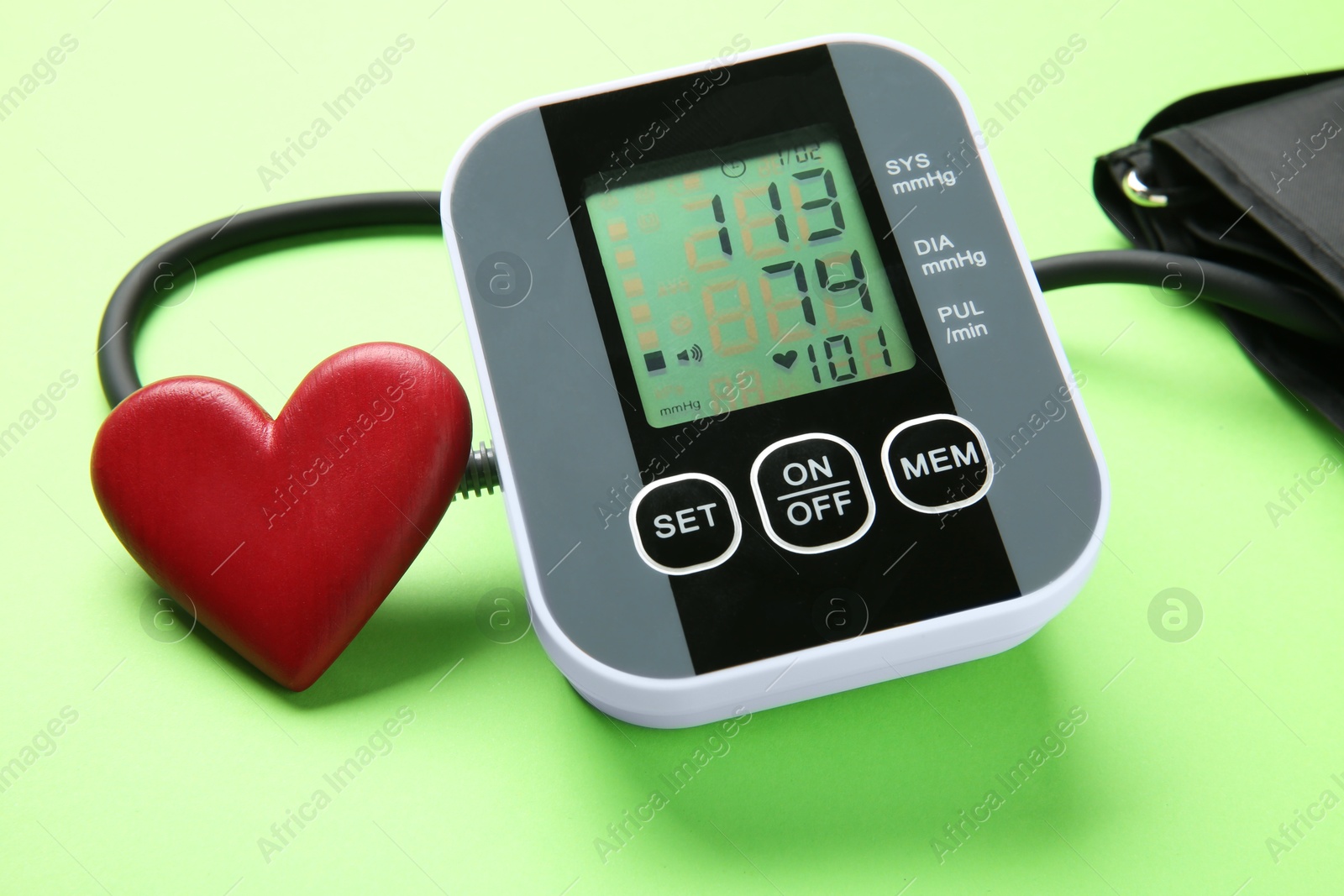 Photo of Blood pressure measuring device and heart figure on green background, closeup