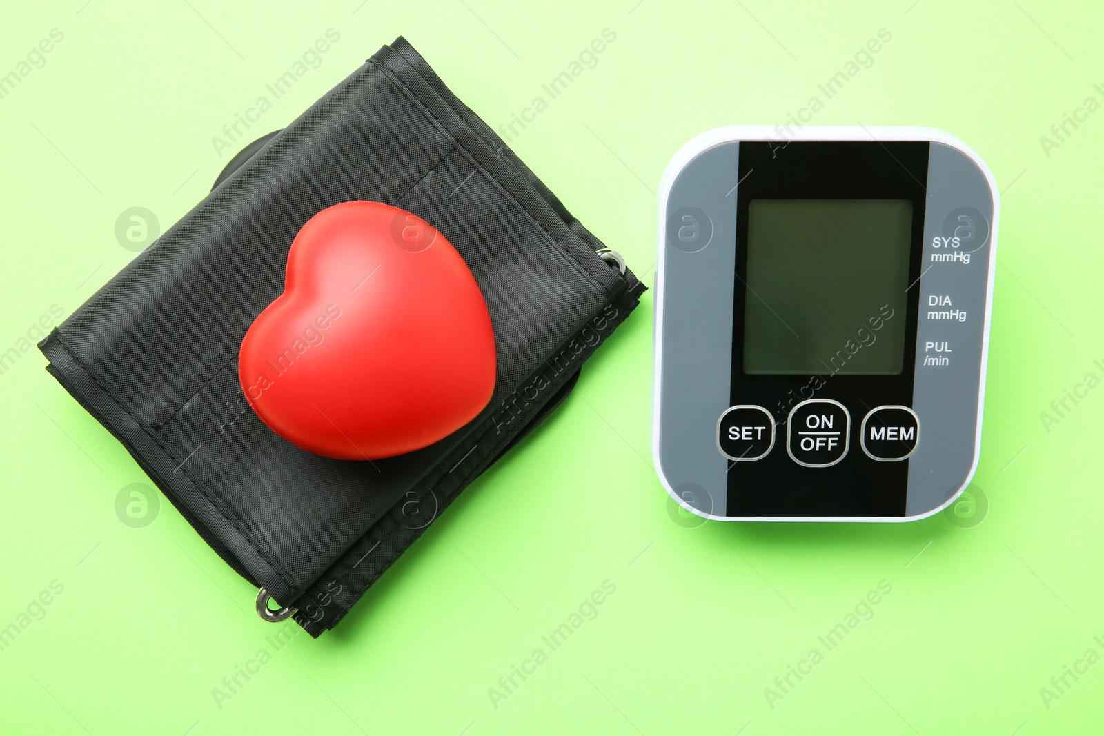 Photo of Blood pressure measuring device and squeeze heart on green background, top view