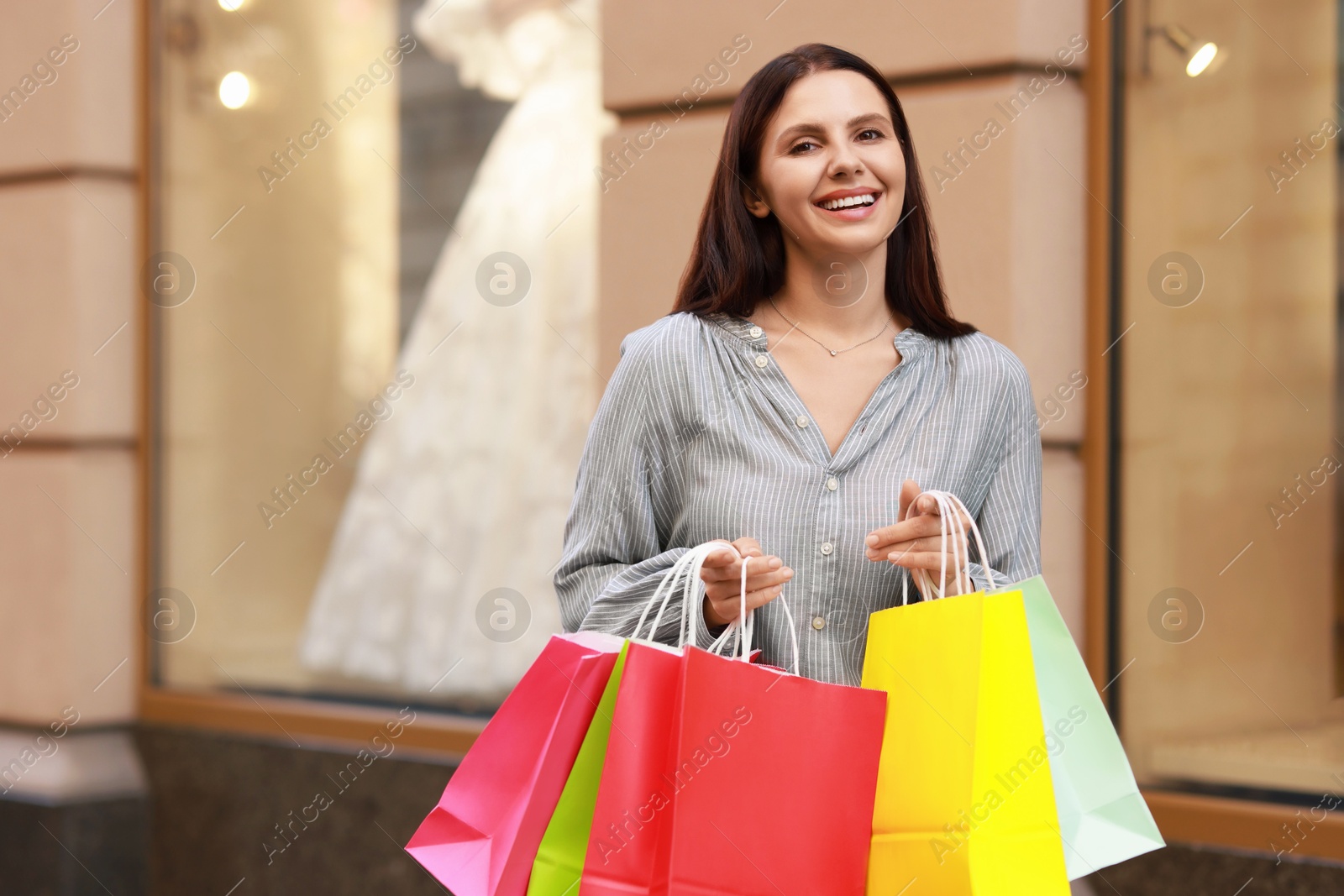 Photo of Happy woman with colorful shopping bags outdoors, space for text