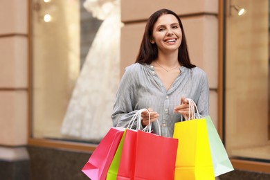 Happy woman with colorful shopping bags outdoors, space for text