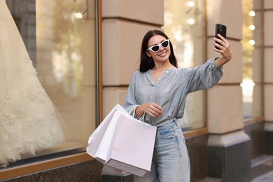 Happy woman with shopping bags taking selfie outdoors