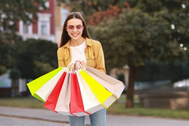 Happy woman with colorful shopping bags outdoors, space for text