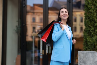 Happy woman with colorful shopping bags outdoors, space for text