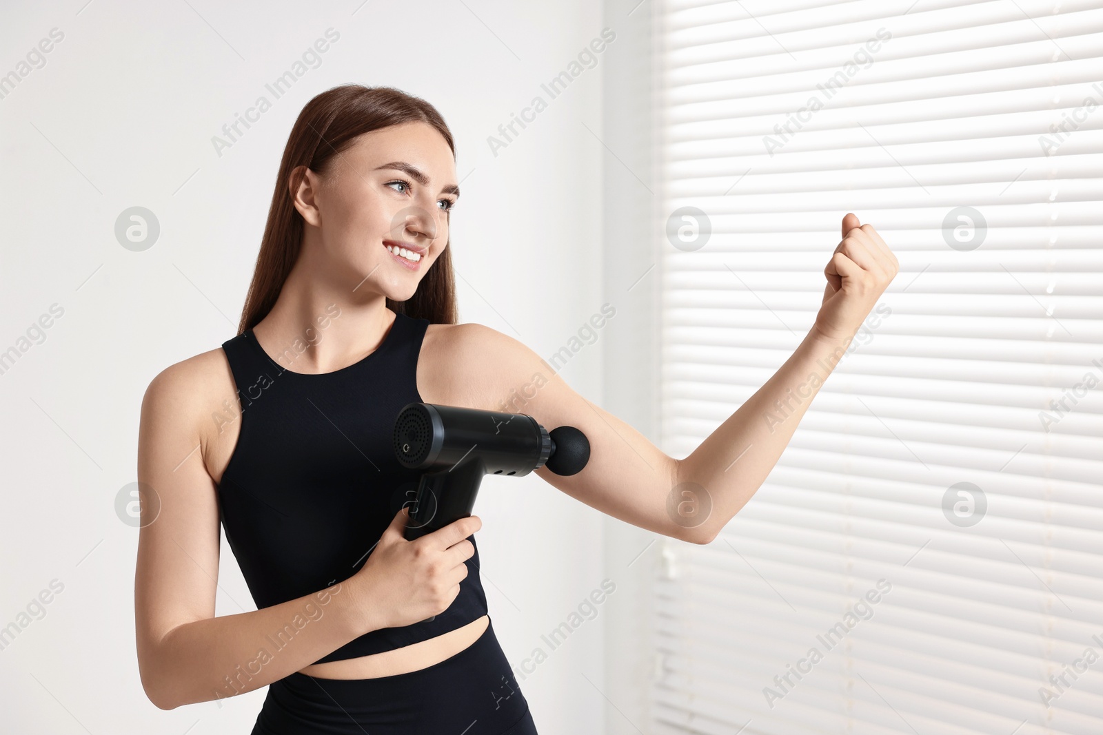 Photo of Woman using percussive massager to relax bicep indoors