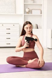 Woman using percussive massager to relieve arm muscles on mat at home