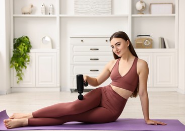 Woman using percussive massager to relieve hip muscles on mat at home