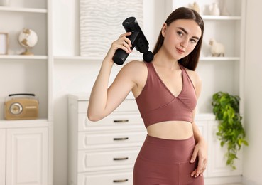 Photo of Woman using percussive massager to relieve trapezius muscle at home