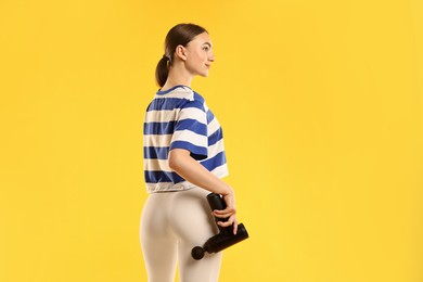 Woman using percussive massager to relax buttock muscles on yellow background