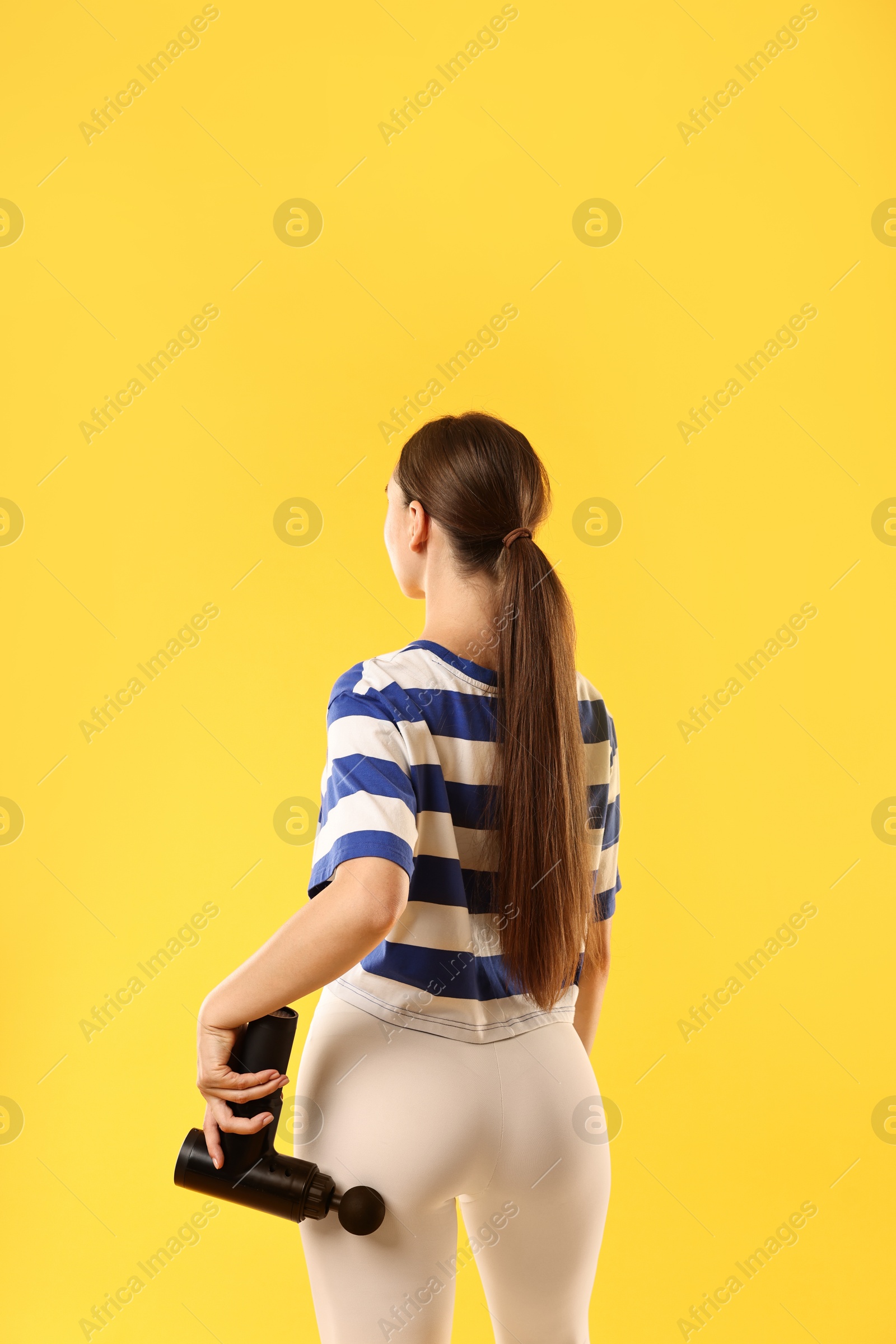 Photo of Woman using percussive massager to relax buttock muscles on yellow background, back view