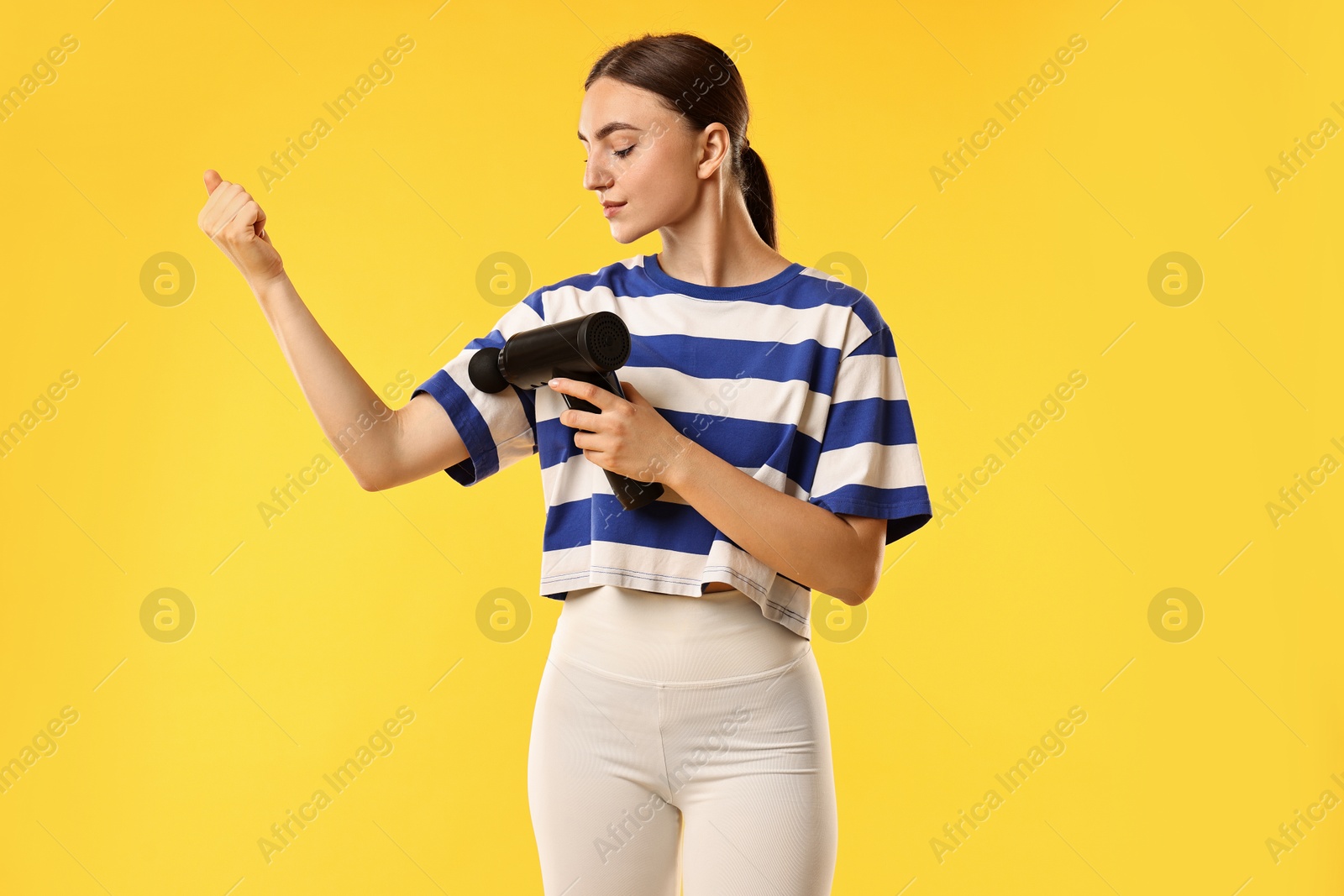 Photo of Woman using percussive massager to relieve bicep on yellow background