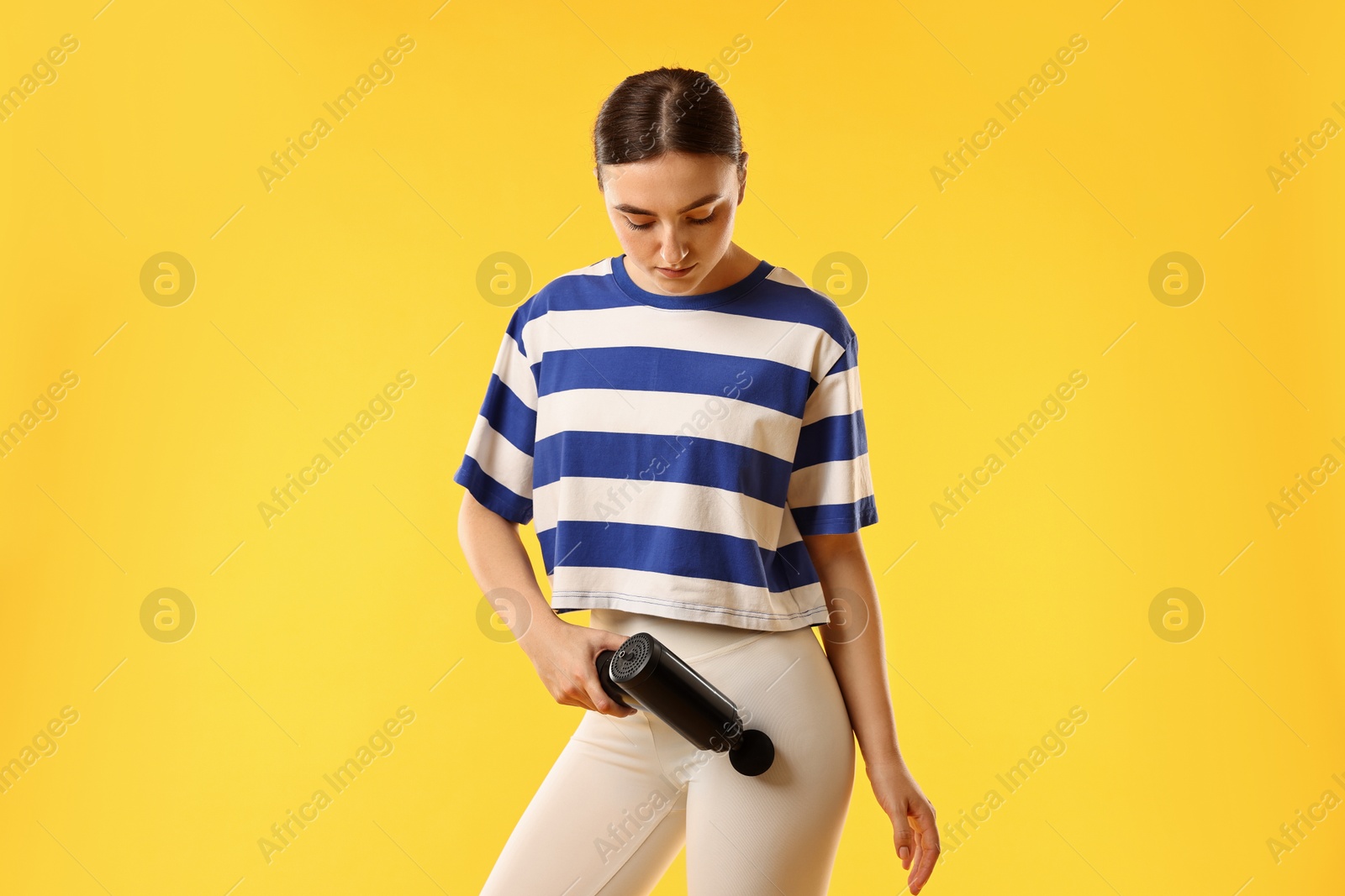 Photo of Woman using percussive massager to relax hip muscles on yellow background