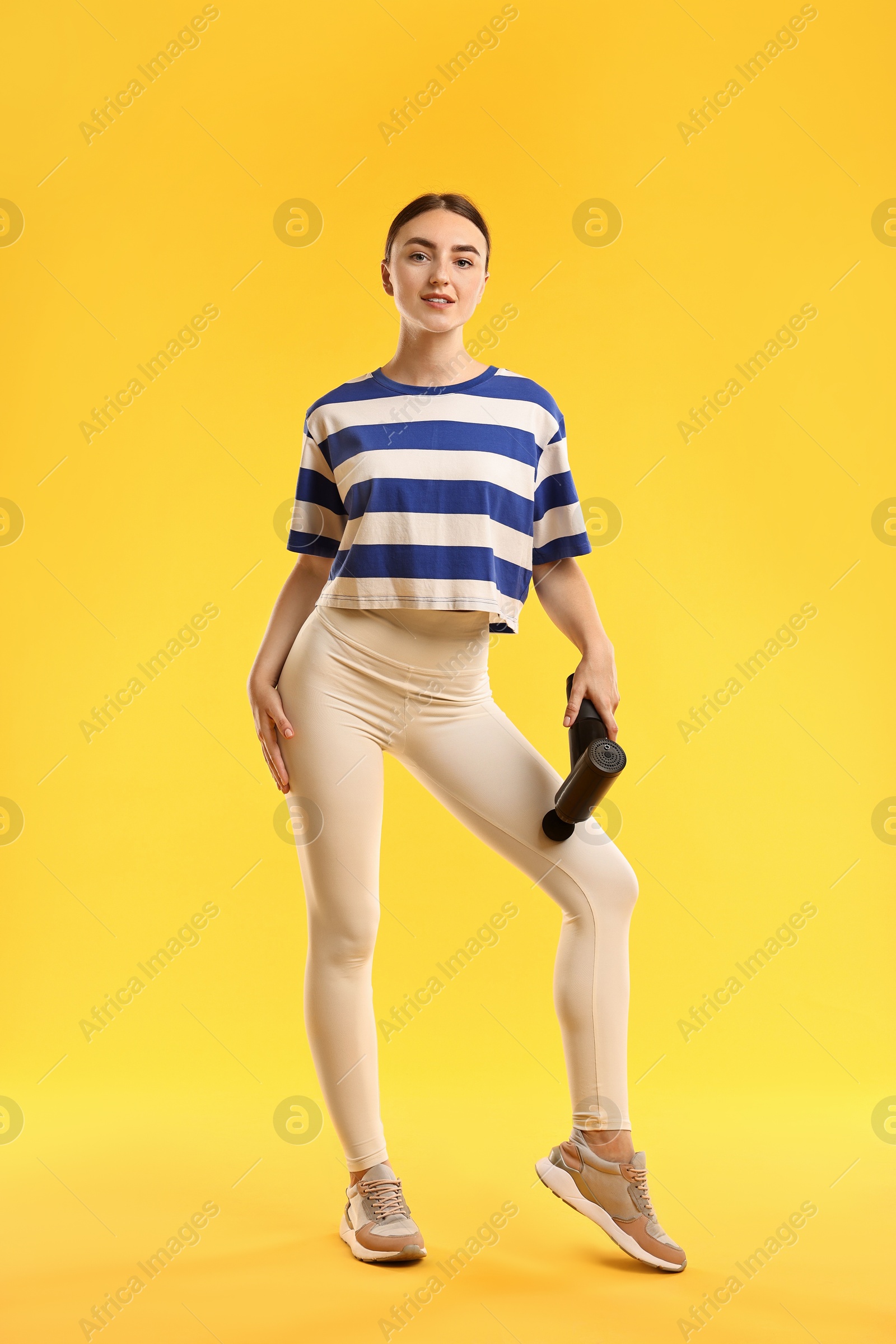 Photo of Woman using percussive massager to relax thigh muscles on yellow background