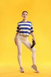 Photo of Woman using percussive massager to relax thigh muscles on yellow background