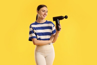 Photo of Young woman with percussive massager on yellow background