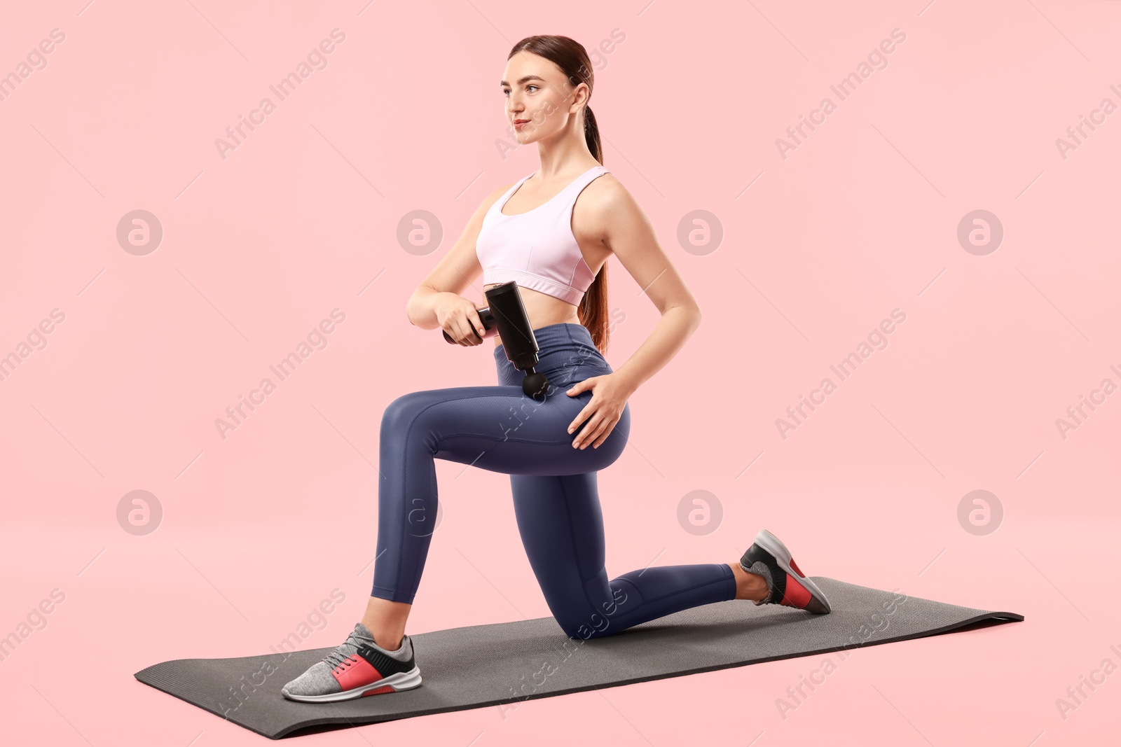 Photo of Woman using percussive massager to relax hip muscles on mat against pink background