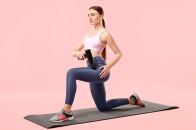 Woman using percussive massager to relax hip muscles on mat against pink background