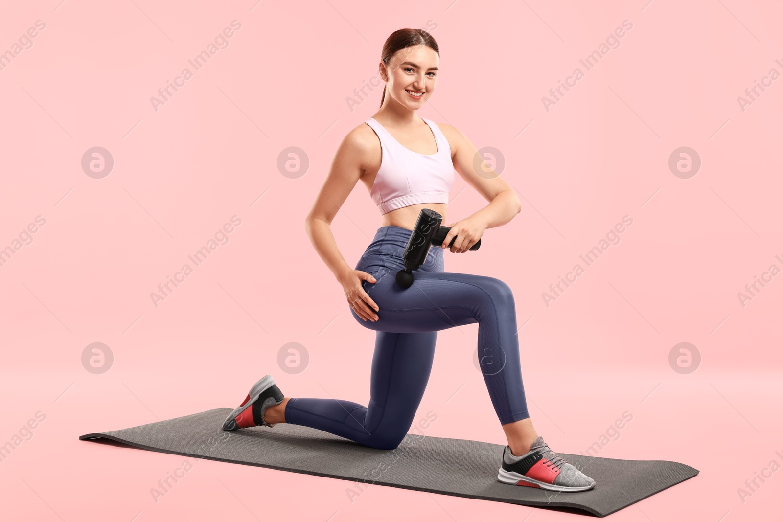 Photo of Woman using percussive massager to relax hip muscles on mat against pink background