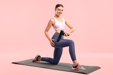 Photo of Woman using percussive massager to relax hip muscles on mat against pink background