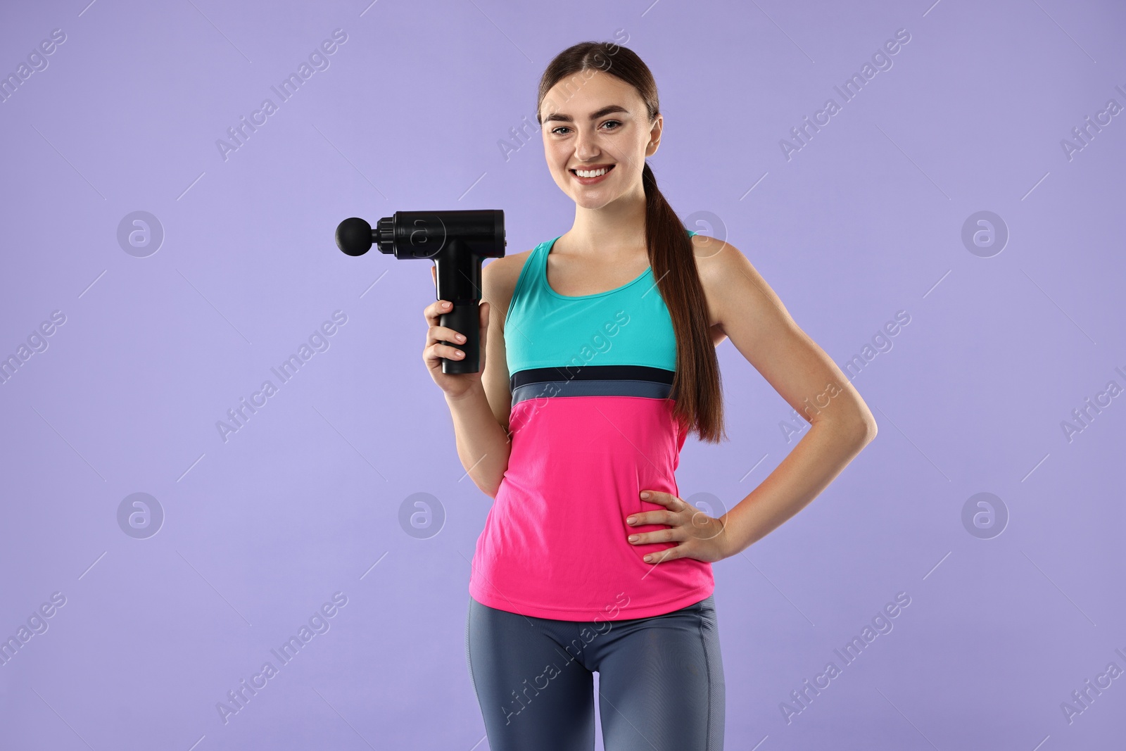 Photo of Young woman with percussive massager on light purple background