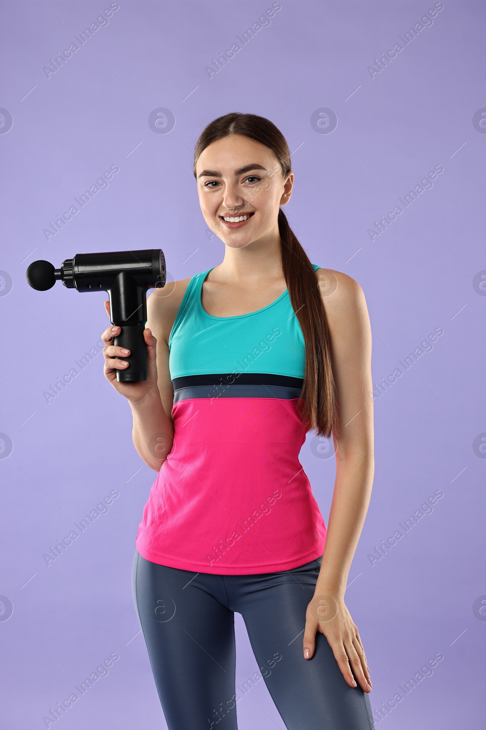 Photo of Young woman with percussive massager on light purple background