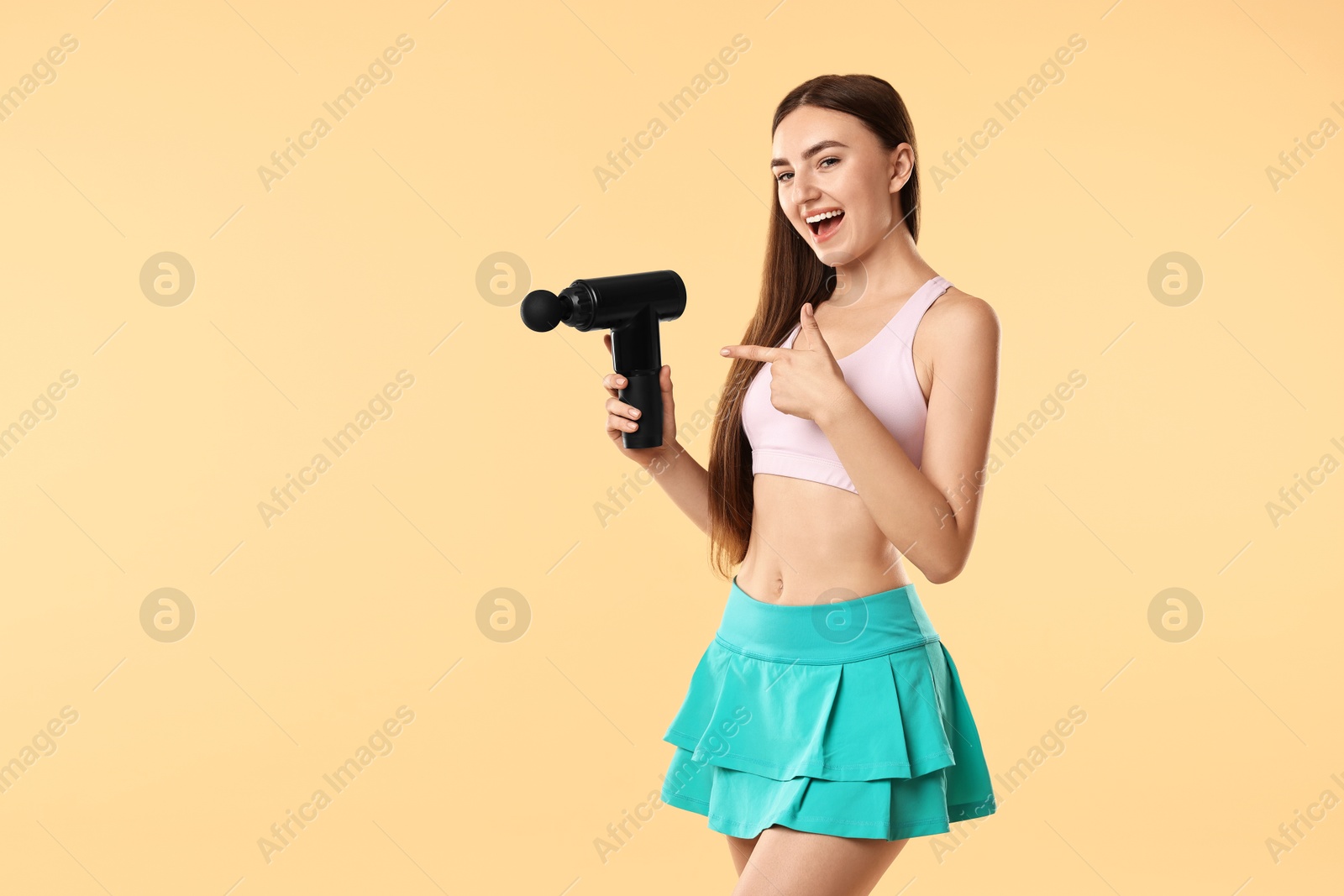 Photo of Young woman pointing at percussive massager on beige background. Space for text