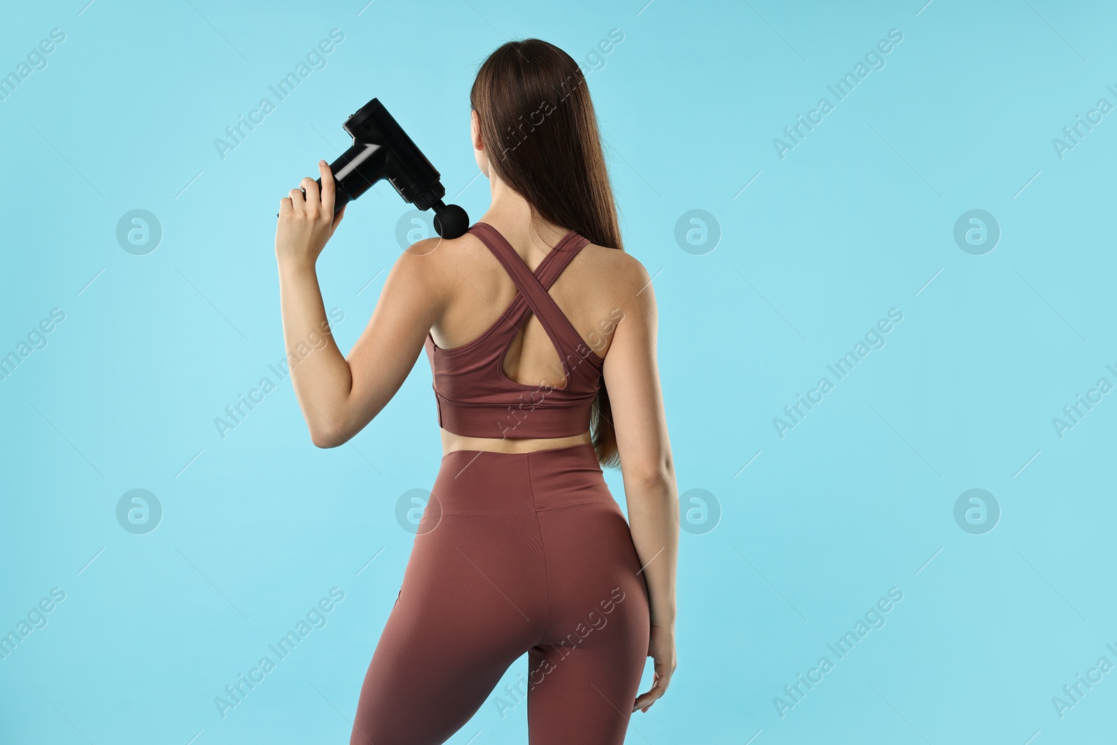 Photo of Woman using percussive massager to relieve trapezius muscle on light blue background, back view