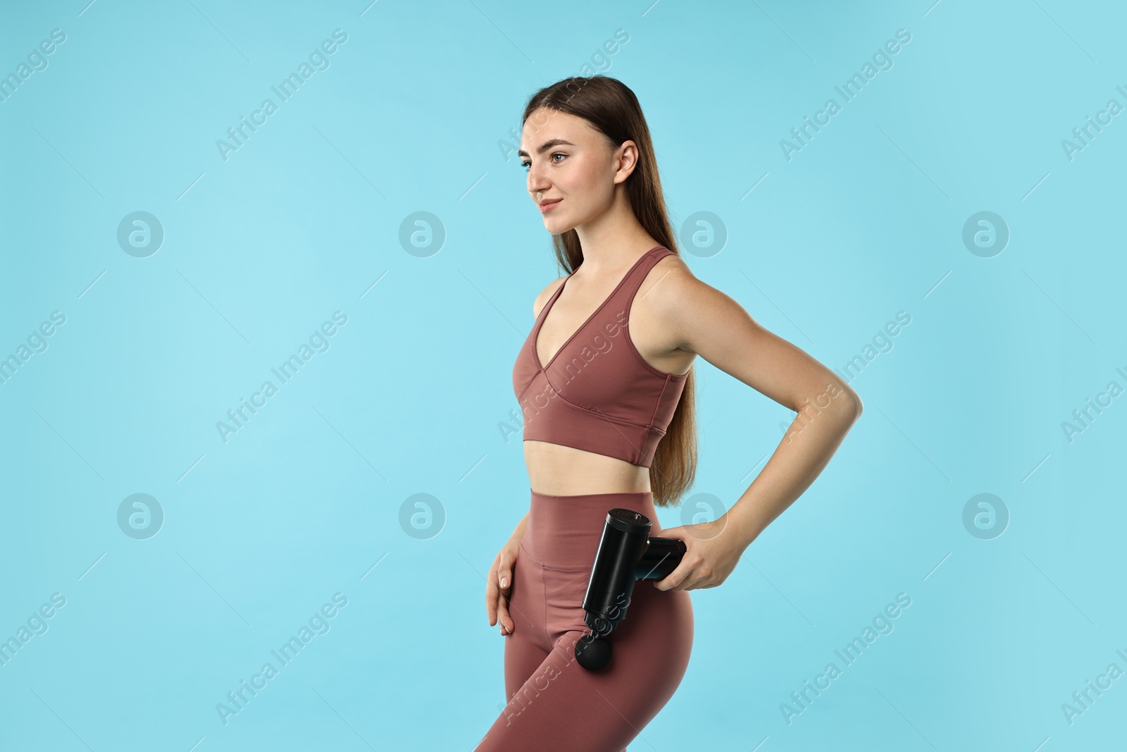 Photo of Woman using percussive massager to relax hip muscles on light blue background