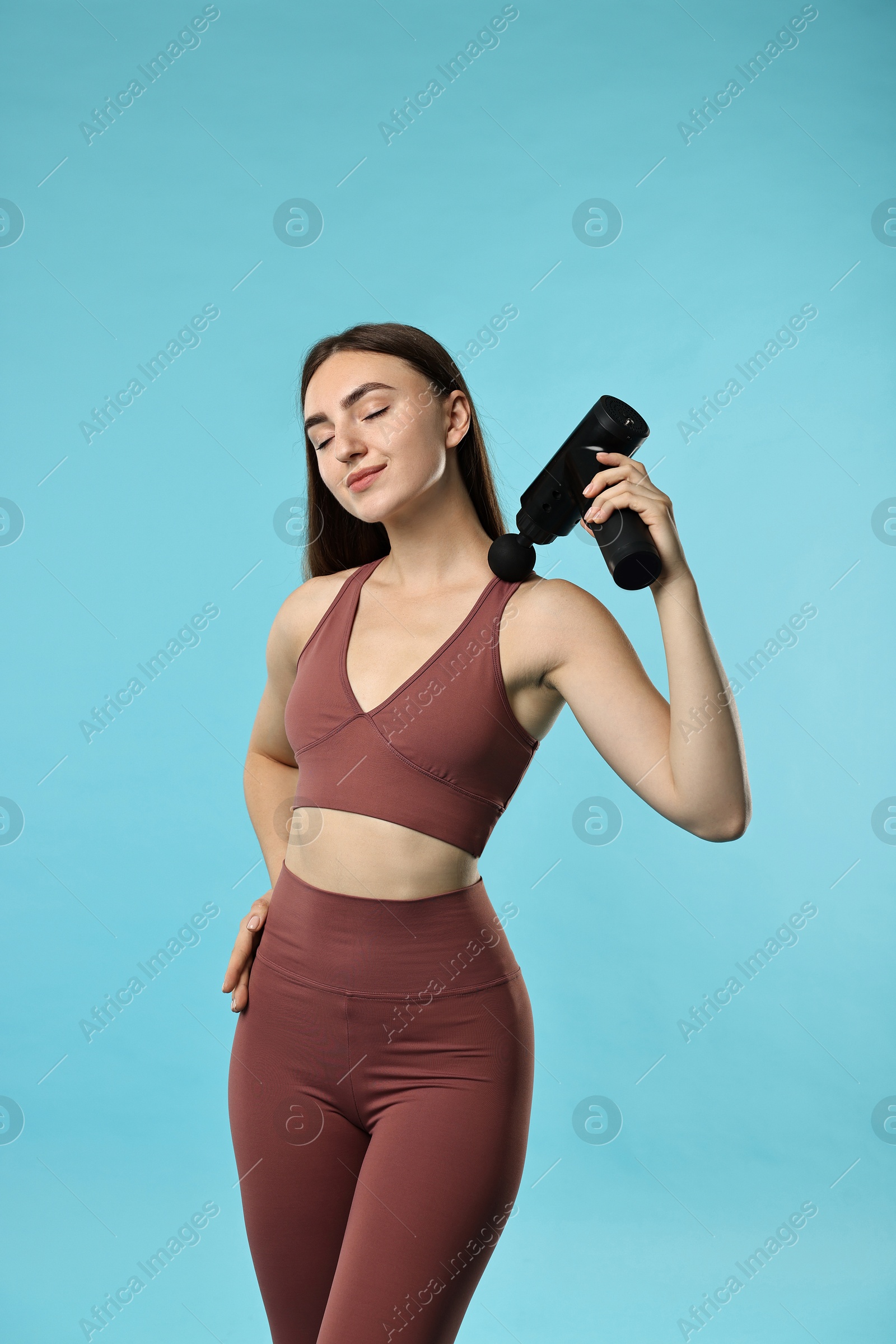 Photo of Woman using percussive massager to relieve trapezius muscle on light blue background