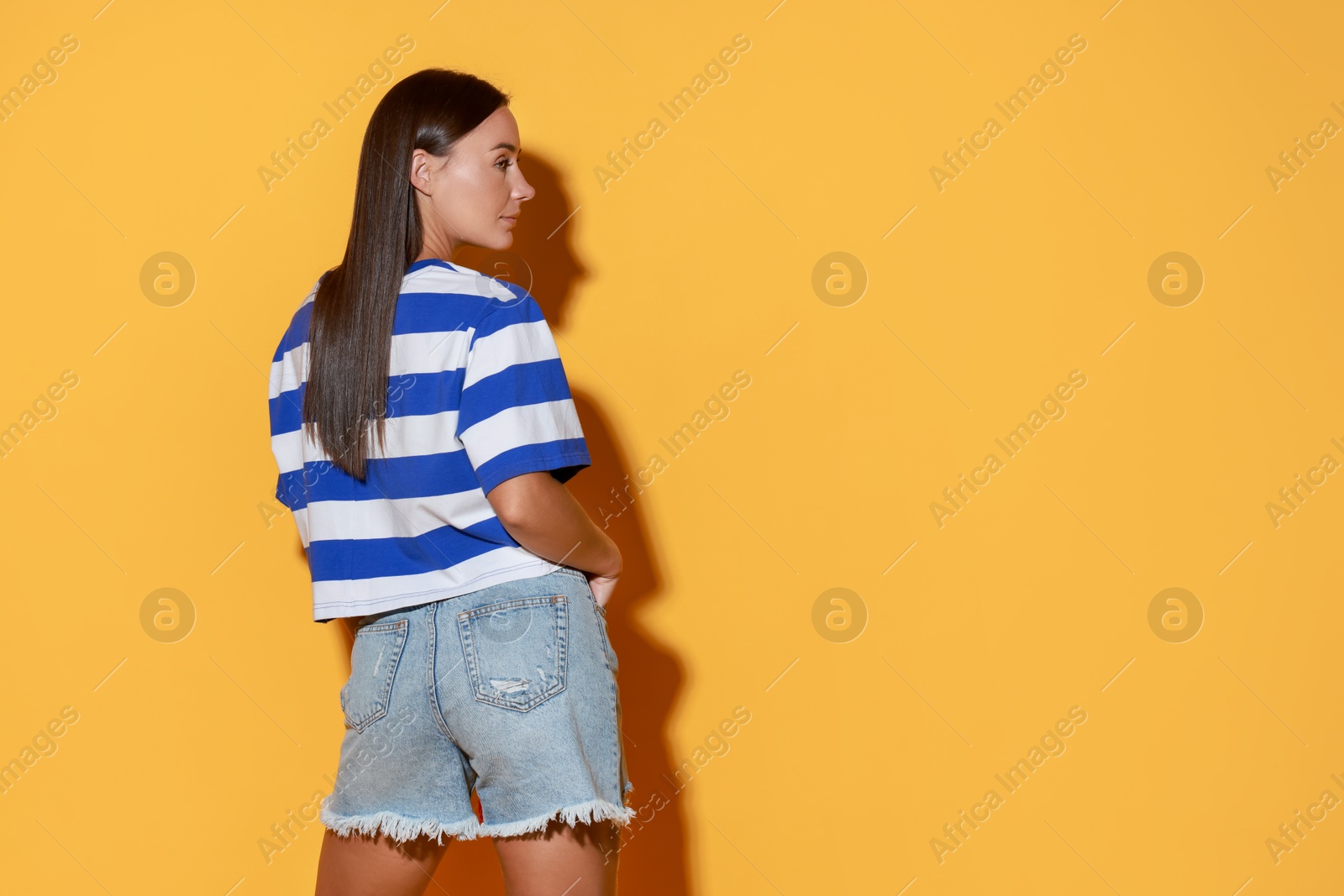 Photo of Beautiful woman wearing stylish denim shorts on yellow background, space for text