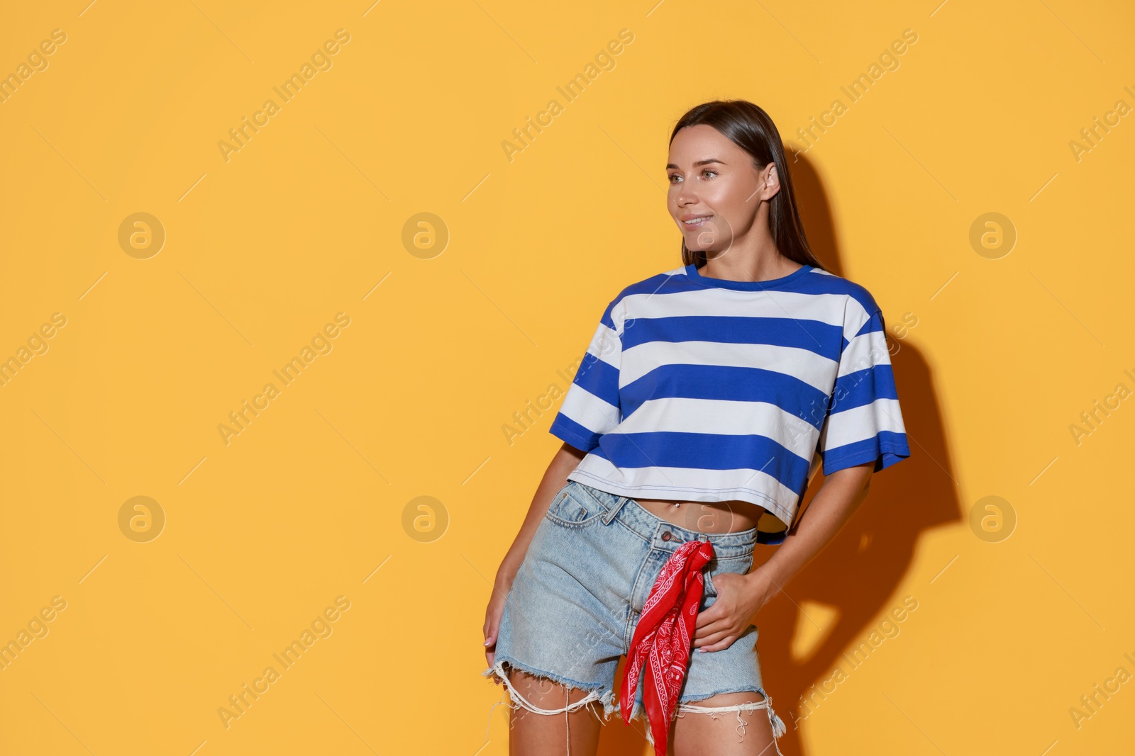 Photo of Beautiful woman wearing stylish denim shorts on yellow background, space for text